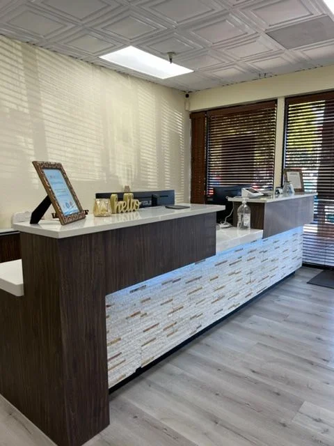 Natomas Dental's front desk: a dark wood counter with a stone-tile front, lit by sunlight through window blinds